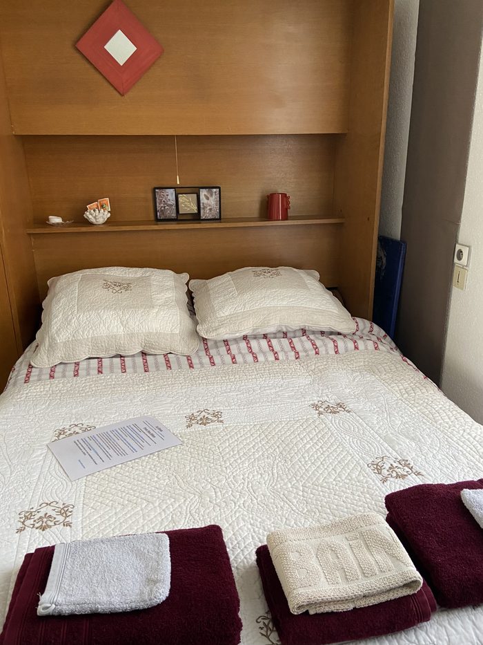 Chambre Brimbelle : lit double encastré sous une tête de lit à niche en bois, couvre-lit matelassé blanc brodé.