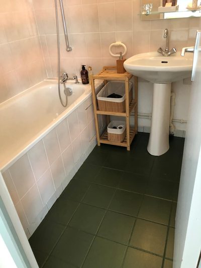 Salle de bains de Fougère : sol vert, baignoire, lavabo sur colonne et étagère à serviettes.
