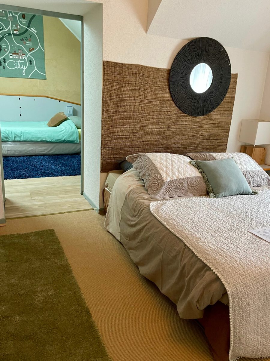 Suite Sapin : lit double habillé d'un couvre-lit rayé, tête de lit en fibre tressée, serviettes de toilette pliées au pied du lit.
